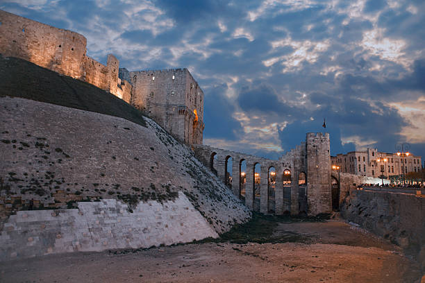 The ancient Aleppo Citadel in Syria illuminated at dusk under a dramatic cloudy sky
