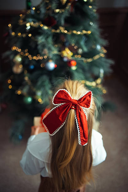 istock Young Girl with Red Bow Admiring a Decorated Christmas Tree 2233589478