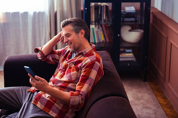 istock Cheerful Man Relaxing on Couch Using Smartphone in Cozy Living Room 2233589623