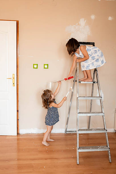 istock Two Girls Helping to Paint Room with White Wall Paint 2233590063