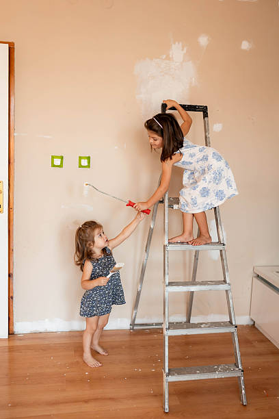 istock Two Girls Helping to Paint Room with White Wall Paint 2233590064