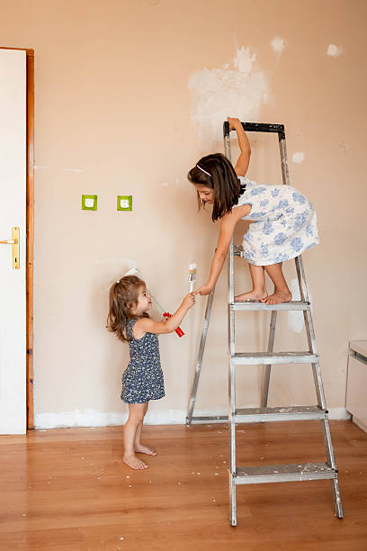 istock Two Girls Helping to Paint Room with White Wall Paint 2233590068