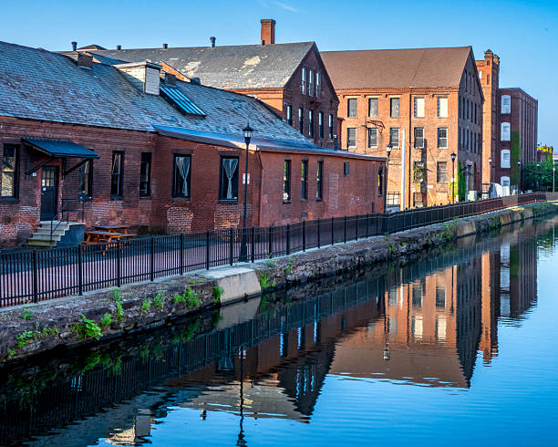 Holyoke, MA - US - Aug 24, 2025 Industrial brick buildings reflecting in a calm canal under a clear sky, showcasing historic architecture and waterfront tranquility.