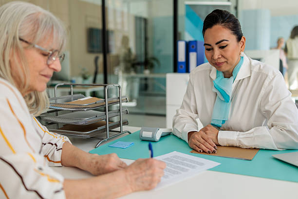 istock Senior Client Signing Agreement with Female Advisor in Bank 2233596050