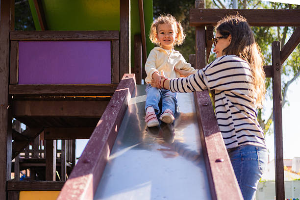 istock Mother helping daughter sliding down playground slide 2233597919