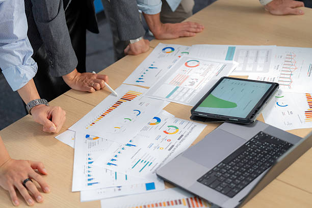 istock Close-up of financial graphs and documents on desk with computer as employee points during discussion. Business meeting, teamwork, strategy, investment, planning, analyzing, and cooperation for success. 2233606392