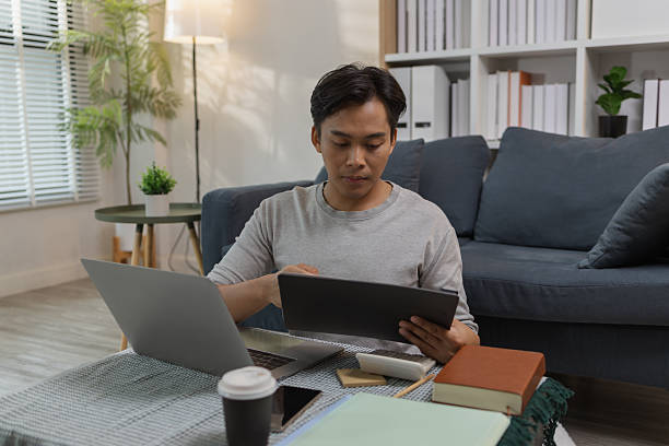 istock A young man is sitting on the floor at home, checking documents while working with his laptop. He appears focused and engaged, managing his tasks in a relaxed modern living space. 2233613861
