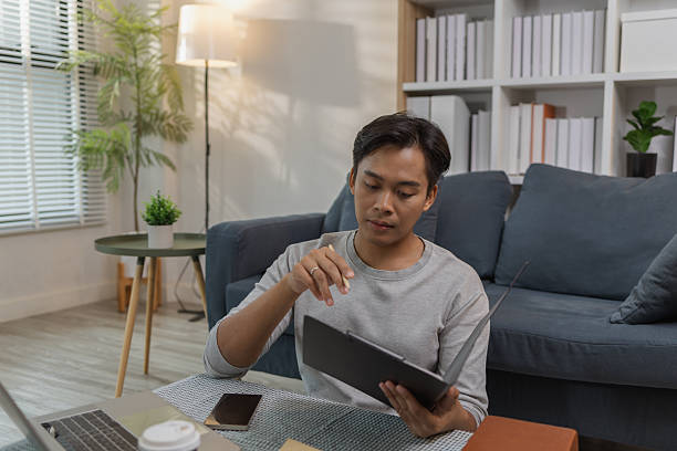 istock A young man is sitting on the floor at home, checking documents while working with his laptop. He appears focused and engaged, managing his tasks in a relaxed modern living space. 2233613896