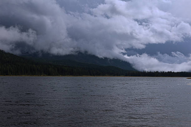 A serene lake scene under a dramatic sky, where dark clouds loom over the mountains, creating a captivating and moody atmosphere.