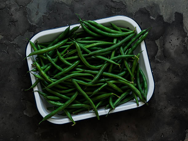 Fresh green string beans in a metal container on a dark background, top view