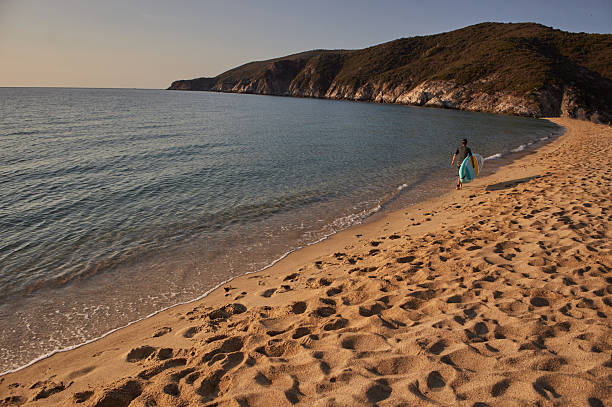 A man is walking on the beach with his surfboard, enjoying life, ready to surf. Copy space.