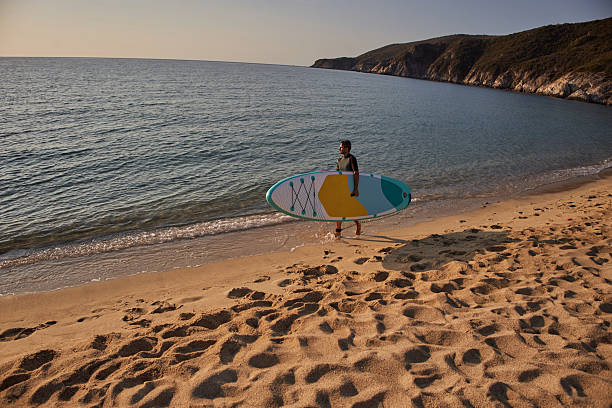 A man is walking on the beach with his surfboard, enjoying life, ready to surf. Copy space.