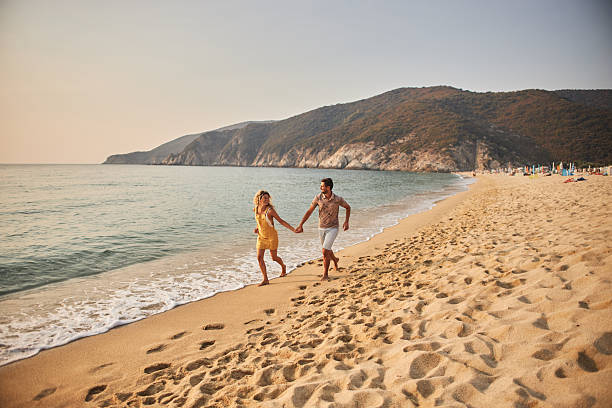 Young couple running hand in hand down a tropical paradise beach during sunset.