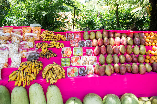 A colorful outdoor fruit stand displays mangoes, bananas, watermelon, and packaged snacks.