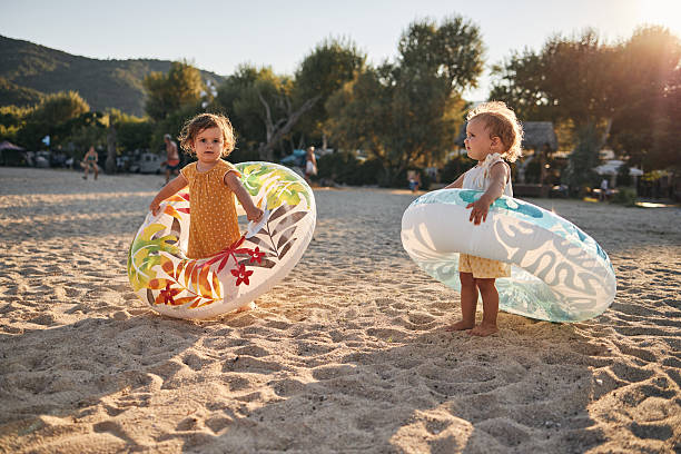 Beautiful twin sisters enjoying sunset on a beach vacation, playing with swimming floats..