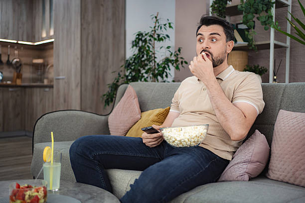 istock Man watching tv and eating popcorn on the sofa at home 2233627095