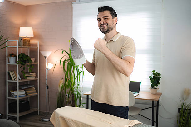 Young man ironing clothes at home, celebrating his achievement