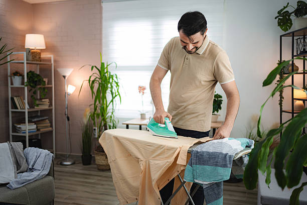 istock Man diligently ironing clothes on ironing board in living room 2233627197