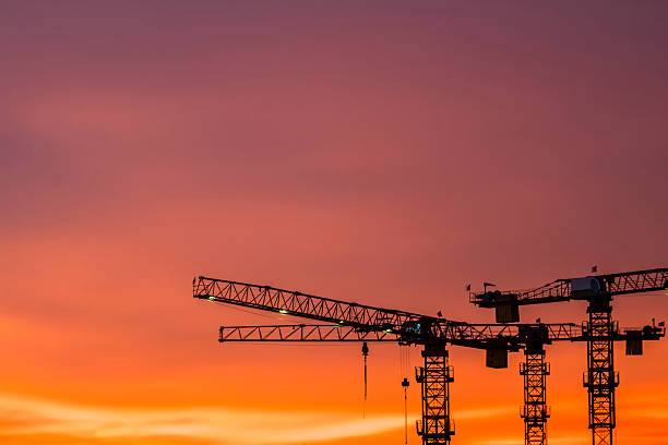 Construction Crane equipment and machinery In Singapore building and construction site against dramatic warm burning sky at dusk