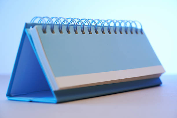 Red notebook lies open on a wooden desk, featuring sticky notes and a manuscript, suggesting organized planning and productivity