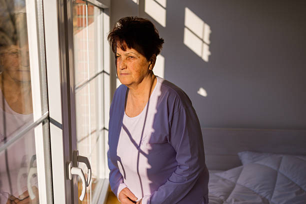 istock Elderly lady gazing through large window in comfortable sleepwear 2233642049