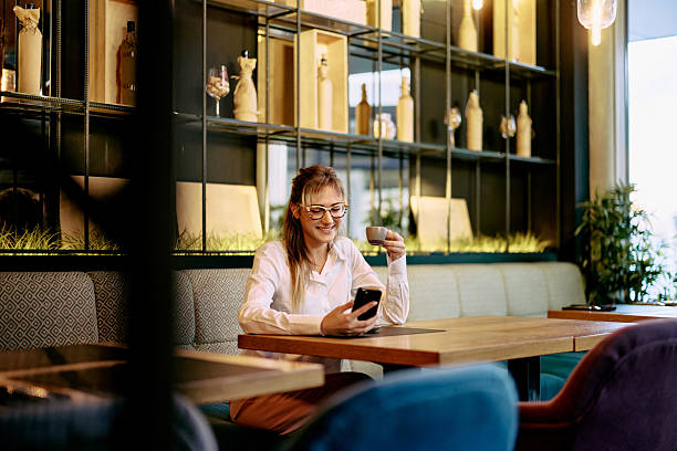 istock Young Woman Enjoying Coffee While Browsing Smartphone at a Modern Cafe 2233643497