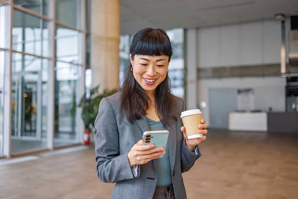 istock Businesswoman using smartphone and holding coffee in office lobby 2233644513