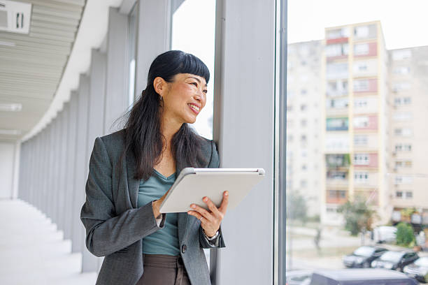 istock Smiling businesswoman using digital tablet looking out office window 2233644909