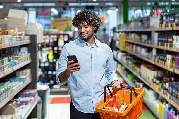 istock A young man smiles while using his phone and shopping at the grocery store. 2233645542