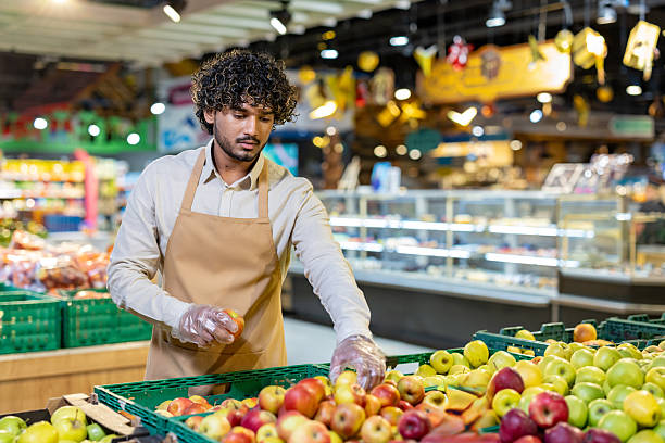 istock A grocery worker meticulously examines fresh apples while stocking the produce section. 2233645596