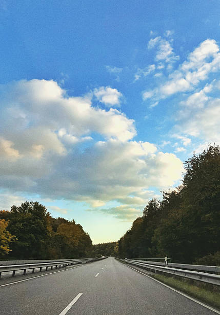Empty road view from a car with autumn forest and blue sky with clouds, natural background