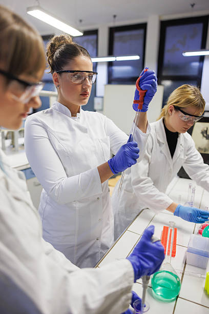 istock Female students wearing lab coats, protective eyewear and gloves practicing in lab with chemicals 2233649834
