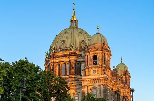 Germany, Berlin, Berlin Cathedral, August 19, 2025 - The Berlin Cathedral in the evening light with tree against clear sky
