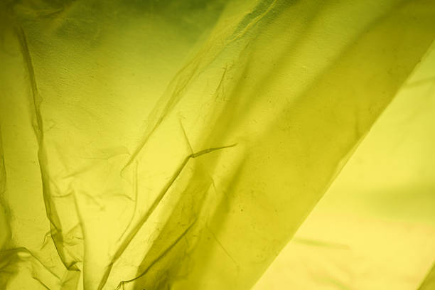Extreme close up of yellow empty plastic bag background. The plastic surface is wrinkly and tattered making abstract pattern. Selective focus, shallow depth of field.
