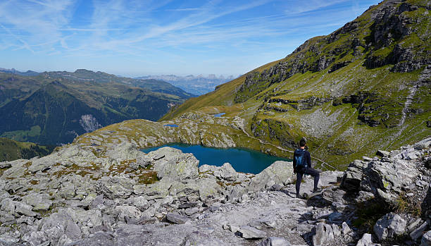 istock Adventurous hiker standing on rocky terrain overlooking a serene mountain lake, surrounded by lush greenery and majestic peaks under a clear blue sky, capturing the essence of exploration 2233657431