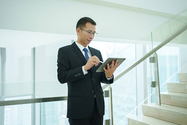 istock Mature Asian businessman standing on stairs and using tablet 2233658240