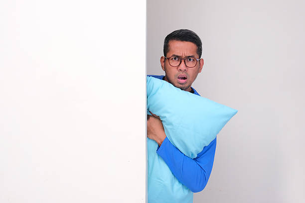 istock Adult asian man peeking behind a wall hugging pillow with curious face expression 2233659378