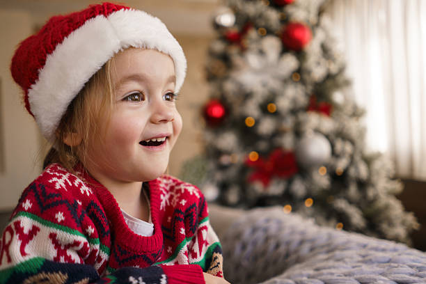 istock Smiling child wearing santa hat looking at christmas tree 2233661458
