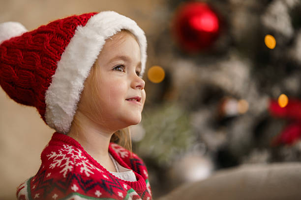 Dreaming child wearing santa hat looking up at christmas tree