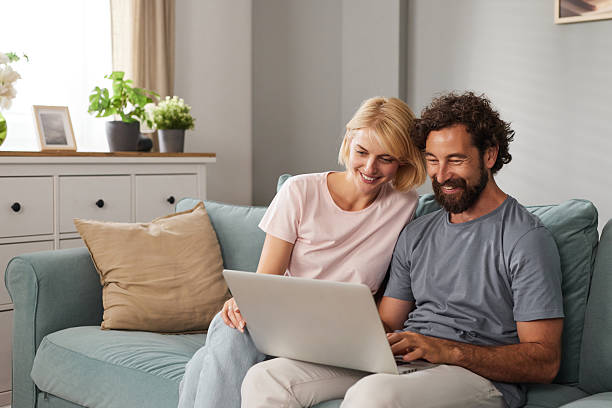 istock Couple happily working together at home on a laptop while sitting on a cozy 2233664336