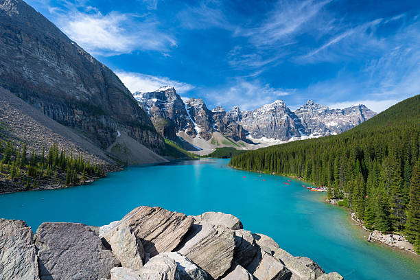A breathtaking view of Moraine Lake in Banff National Park, Alberta, Canada. The iconic turquoise waters are surrounded by the rugged peaks of the Canadian Rockies and dense evergreen forests. A world-famous travel destination symbolizing Canada travel, adventure, and pristine mountain landscapes. Perfect for themes of exploration, nature, road trips, and iconic scenic destinations.
