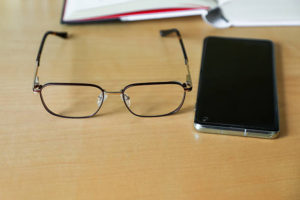 Reading glasses and a smartphone rest on a wooden table next to an open book, creating a cozy and inviting scene perfect for education, study, or home comfort imagery.