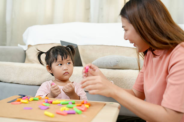 istock Asian single mother and little daughter sitting together learning creative clay modeling on table in cozy bright home living room early childhood education observing and practicing skills 2233676421