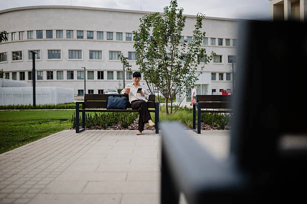 istock Japanese Businesswoman Sitting on Bench, Using Smartphone and Drinking Coffee During Break 2233677601