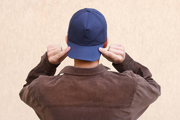 Man in stylish baseball cap near beige wall, back view. Mockup for design