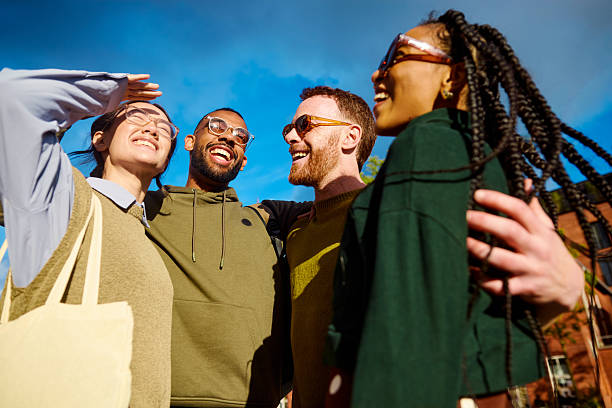 Four cheerful diverse gen z university students walking and smiling outdoors on a sunny day