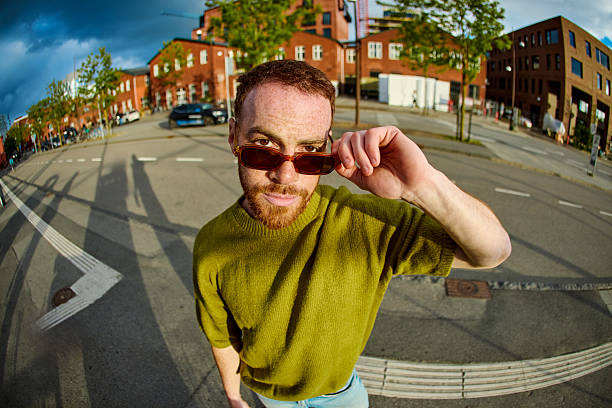 Portrait of a cheerful young man adjusting his sunglasses while commuting in the city with fisheye lens