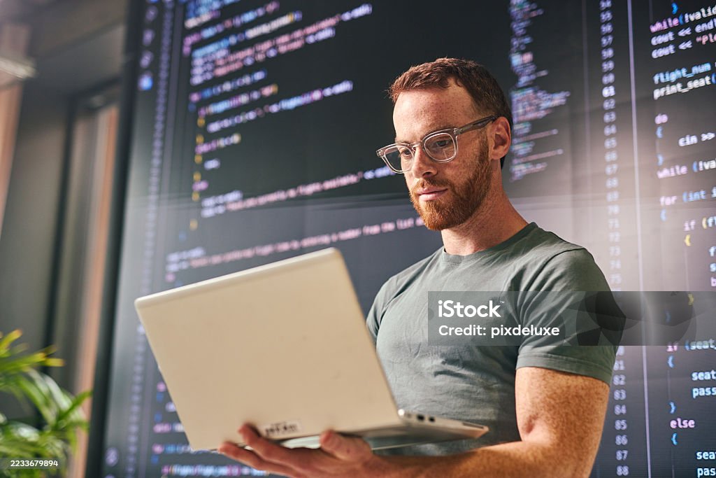 Focused software developer working on laptop with code displayed on screen in modern office Young adult male software developer concentrating on his laptop, with lines of code displayed on a large screen in the background, in a contemporary office setting Artificial Intelligence Stock Photo Focused software developer working on laptop with code displayed on screen in modern office Young adult male software developer concentrating on his laptop, with lines of code displayed on a large screen in the background, in a contemporary office setting Artificial Intelligence Stock Photo