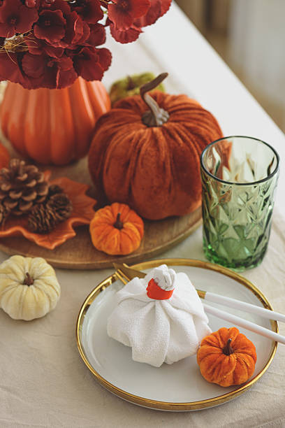 Thanksgiving table setting with decorative pumpkins, candles and string lights on white wooden table