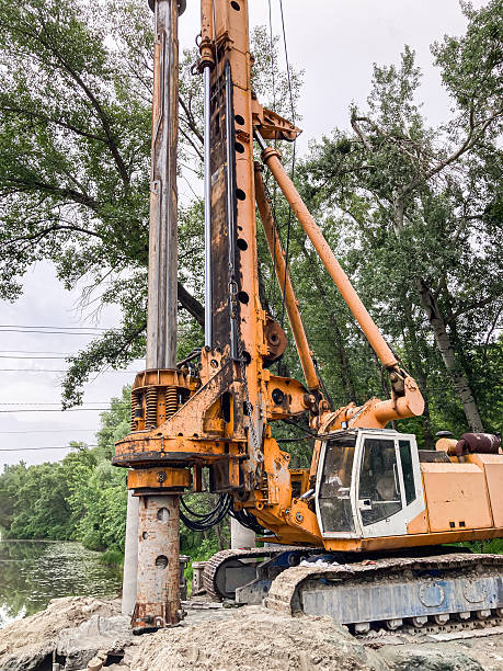 istock Large yellow crane on platformfoundation by water, trees in background, overcast sky, worn appearance, distant figure for scale, daytime, diffused natural light 2233683270
